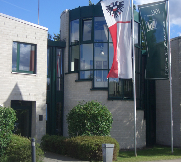 Modernes Bürogebäude mit runder Glasfront und wehenden Flaggen vor dem Eingangsbereich.