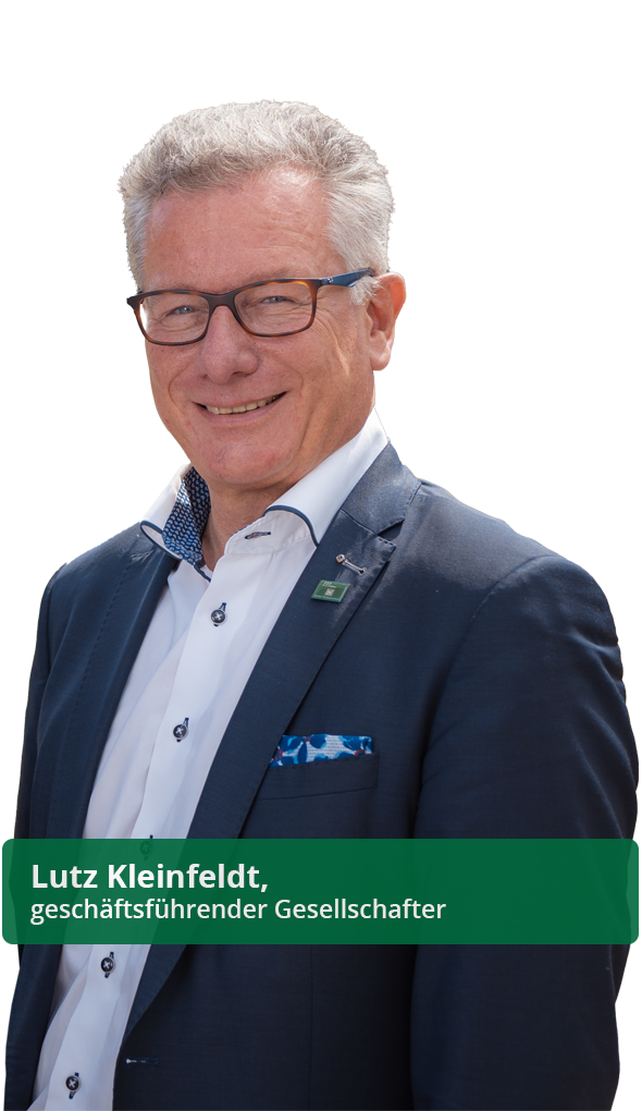 Ein lächelnder Mann mit Brille und grauem Haar trägt ein dunkelblaues Sakko über einem weißen Hemd vor weißem Hintergrund.
