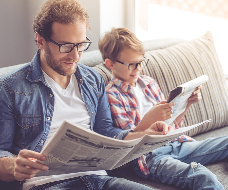 Ein Mann und ein Junge sitzen nebeneinander auf einem Sofa und lesen jeweils eine Zeitung.