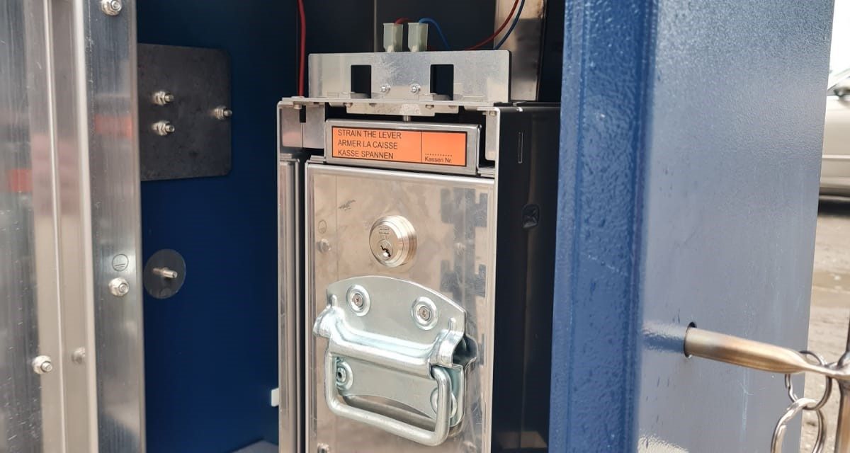 Ein geöffneter blauer Parkscheinautomat mit einer herausnehmbaren Geldkassette aus Metall und einem Schlüsselbund an der Seite.