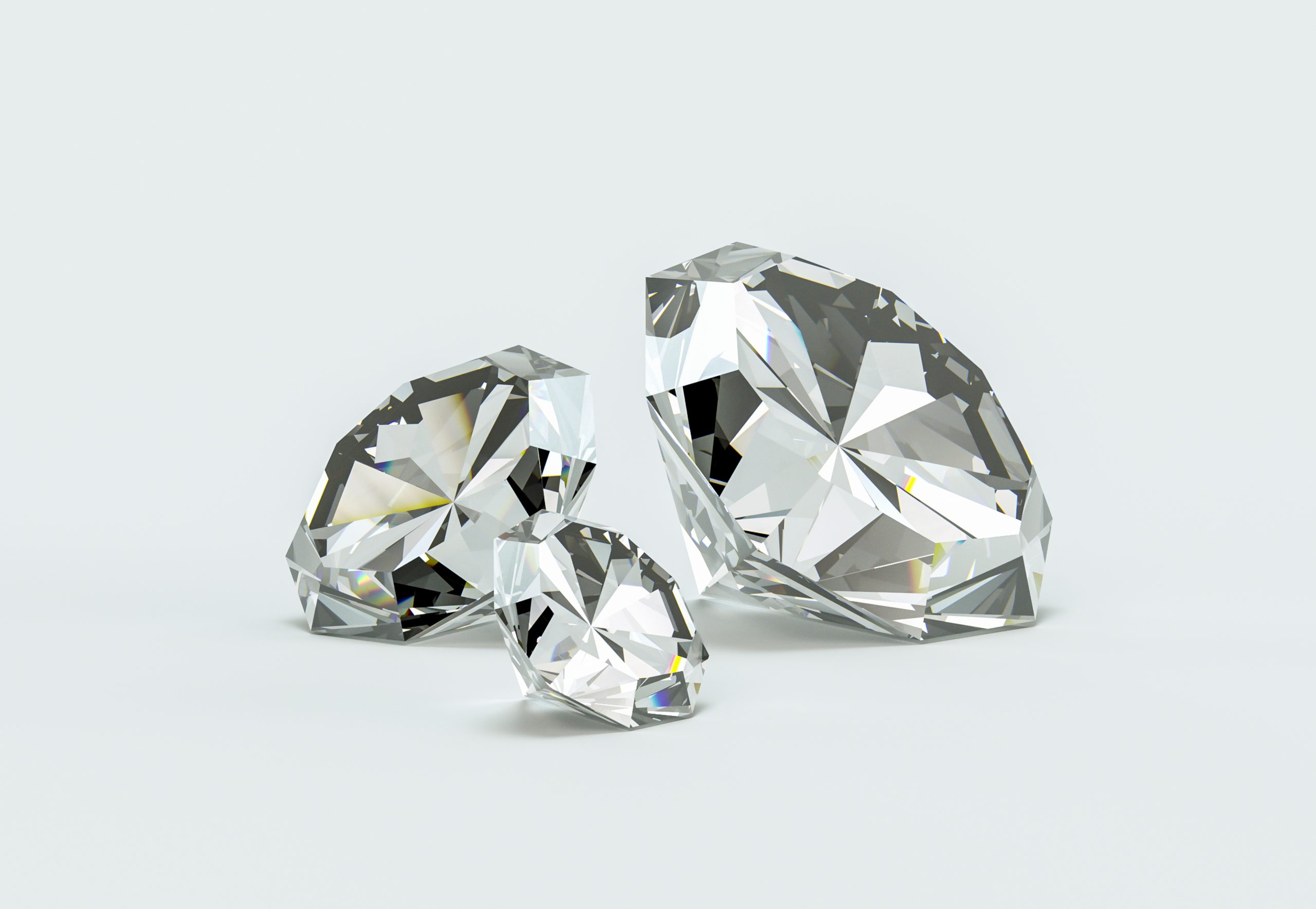 Drei geschliffene Diamanten in unterschiedlichen Größen auf einem hellen Hintergrund.