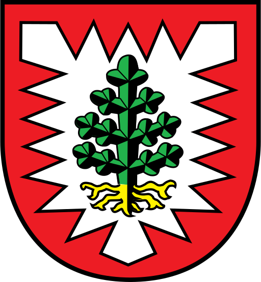 Ein rotes Wappenschild mit einem weißen Nesselblatt, in dessen Mitte eine stilisierte grüne Tanne mit gelben Wurzeln steht.